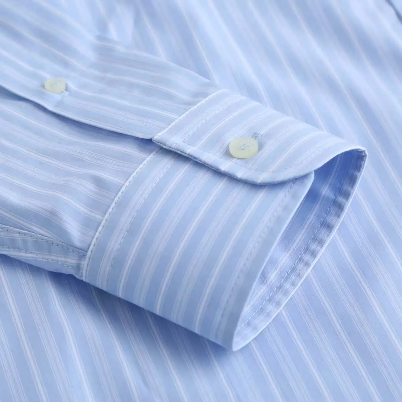 AMI Embroidered Striped Shirt Fabric Selection: Made of 100% cotton poplin fabric. The pure cotton fiber can quickly absorb moisture and perspire, making it refreshing and not stuffy when worn for a long time. The unique plain weave process of poplin makes the fabric both soft and skeletal, not easy to wrinkle and deform, and the upper body is neat and clean. Coupled with the fine blue and white stripes all over the body, the light color scheme is gentle and elegant, which can meet the needs of different scenes. Process 1: Accurately mark the embroidery position on the chest patch pocket to ensure that the pattern does not shift and does not destroy the overall beauty of the striped fabric. High-count embroidery threads of the same color as the fabric are selected, and flat stitch embroidery technology is used. The stitches are evenly tracked, the edges are clean and neat, and the love outline is simple and smooth. It retains recognition without irritating the skin. It is blended into the striped texture in a low-key manner to avoid an abrupt feeling, while ensuring that the embroidery threads are Wear-Resistant. 2: After the embroidery is completed, perform high-temperature ironing and thread trimming to ensure that the pattern is smooth and compliant, and it is not easy to lose thread or warp after being worn for a long time. Details: 1. The collar seat adopts double-layer reinforcement technology, which is not easy to collapse and deform after long-term wear. The collar corner has a soft arc, which can modify the neck line without being too sharp, making it neat and decent. 2. The inner side of the placket has hidden hemming treatment to avoid burrs on the fabric, while enhancing structural stability and preventing it from deforming after multiple washes. Accessories: One-to-one customized buttons Size: S M L XL Style number: D 236